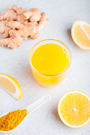 Immune boosting drink with citrus fruits, ginger, turmeric. Drink or smoothie with yellow fall leaves for autumn or virus season on neutral beige background, still lifeの写真素材