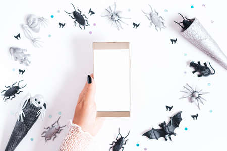 Halloween card on white background with black and silver holiday decor. Woman with black manicure holding silver cone with silver and black bats and ghosts flying around, copy space, top viewの写真素材