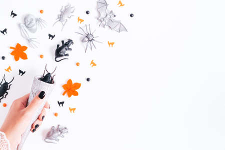 Halloween card on white background with black and silver holiday decor. Woman with black manicure holding silver cone with silver and black bats and ghosts flying around, copy space, top viewの写真素材