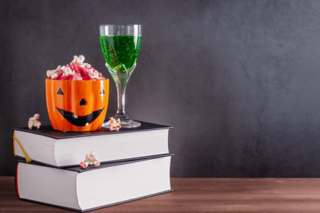 Book stack with popcorn in scary pumpkin orange mug and green cocktail against grey stone background, web banner, copy spaceの写真素材