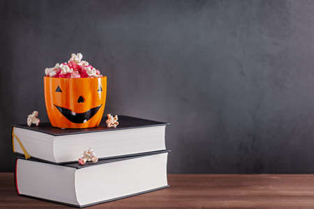 Book stack with popcorn in scary pumpkin orange mug against grey stone background, web banner, copy spaceの写真素材