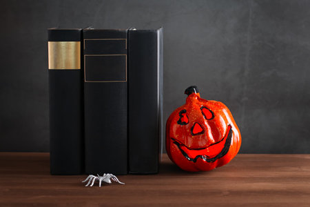 Book stack with scary pumpkin lantern against gray stone background, copy space, still life