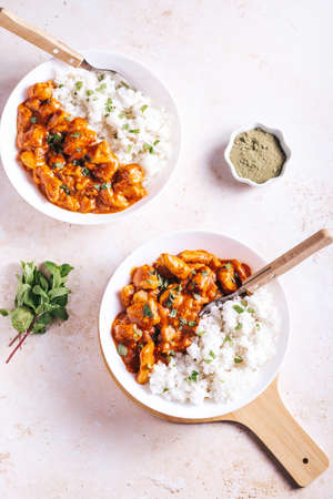 Chicken tikka masala and rice in white bowl on neutral table topの写真素材