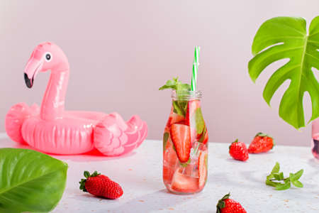Strawberry and mint infused water in glass bottle on table, still life with summer cocktail, monstera leafの写真素材