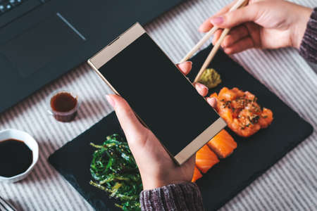 Woman eating sushi takeaway at work desk overhead. Eating sushi for lunch break, lunch meal at workの写真素材
