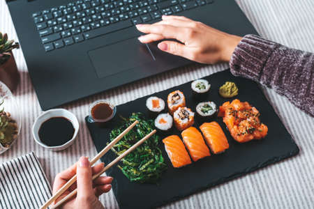 Woman eating sushi takeaway at work desk overhead. Eating sushi for lunch break, lunch meal at workの写真素材