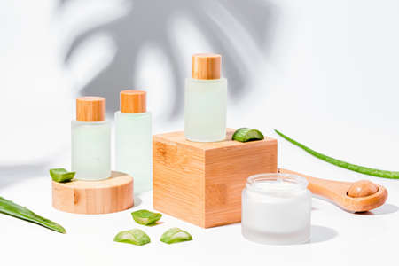Natural cosmetics with aloe on wooden podiums in reusable bottles with plant shadow on backgroundの写真素材