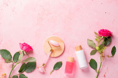 Rose extract natural cosmetics in reusable bottles with gua sha facial beauty roller and natural rose flowers on pink, border with copy spaceの写真素材