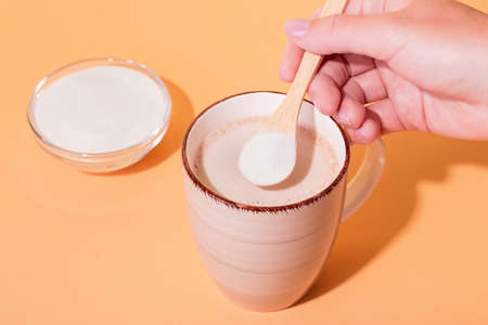 Coffee mug and collagen powder on table in hard light. Bright, minimal composition with hard shadows on colorful background. Woman adding collagen powder to her morning coffeeの写真素材