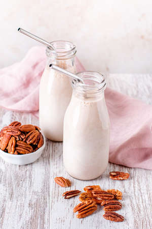 Alternative non dairy homemade pecan milk in glass bottles with reusable metal drinking straws. Pecan nut milk on wooden trayの写真素材