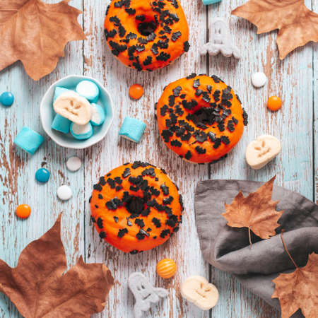 Orange Halloween doughnuts decorated with chocolate bats, licorice lollipops and spooky marshmallows on blue wooden table. Halloween background, flat lay, copy spaceの写真素材