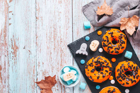 Orange Halloween doughnuts decorated with chocolate bats and spooky marshmallows on blue wooden table. Halloween border, flat lay, copy spaceの写真素材
