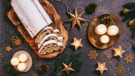 Christmas Stollen cake and golden decor on dark table. Christmas Stollen, burning candles, Christmas tree branches and golden baubles flat lay, top viewの写真素材