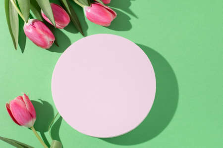 Pink podium for product display on green with tulips flowers in hard lightの写真素材