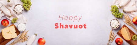 Shavuot flat lay with dairy products, first fruits and wheat on light gray background, web banner. Jewish Shavuot holiday frame with dairy foods and fruits and quote happy Shavuot, top viewの写真素材