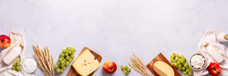 Shavuot flat lay with dairy products, first fruits and wheat on light gray background, web banner. Jewish Shavuot holiday frame with dairy foods and fruits, top viewの写真素材