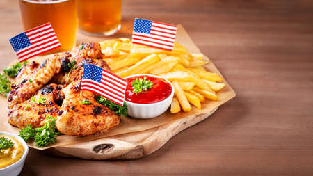 Table with food for USA 4th July Independence Day. Fourth July party or picnic food with chicken wings, fries and beer, decorated with american flags, top view, copy spaceの写真素材