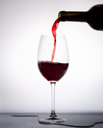 Red wine pouring into a glass from bottle isolated on white background