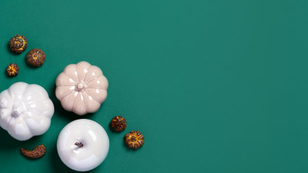 Autumn border with white pumpkins and ceramic decor on dark green background. Fall card in white, green and gold colors, top view, copy space. autumn season web bannerの写真素材