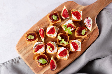 Toasts with figs, ricotta and fig marmalade sprinkled with honey on wooden board, top view. Autumn season snack with fresh produceの写真素材