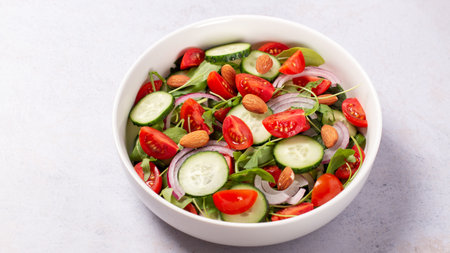 Healthy salad with tomato, cucumber, greens and nuts on light backgroundの写真素材