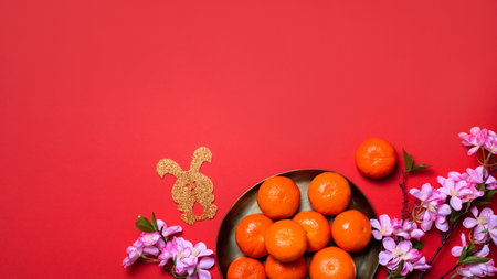 Chinese or lunar new year flat lay with plate of mandarins, paper rabbits as symbol of 2023 and flowers on red, top view, copy space, web banner. Lunar New Year creative flat lay in minimal styleの写真素材