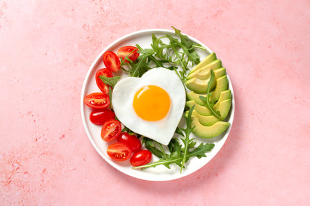 Fried eggs in heart shape, avocado and vegetables in white plate - surprise breakfast for wife or girlfriend on Valentines Day, Womens Day or Mothers Day. women's breakfastの写真素材