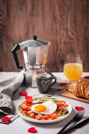 Fried eggs in heart shape, bacon and vegetables, coffee and croissant - surprise breakfast for husband or boyfriend on Valentines or Fathers Day. Men's Breakfast for Valentines Day or Fathers Day holiday.の写真素材