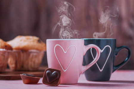 Two coffee cups with heart in pink and black colors standing for female and male gender, muffins and chocolates. valentine's day holiday conceptの写真素材