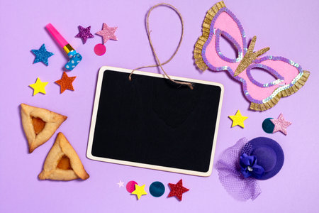 Purim carnival frame with traditional cookies, costume accessories and decor on pastel violet background with black board for text, copy spaceの写真素材