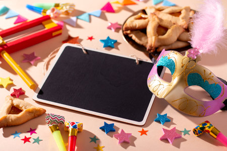 Purim table with hamantaschen cookies, carnival mask, black board for text, holiday decor in hard lightの写真素材