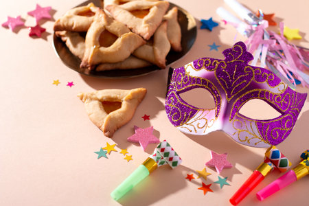 Purim table with hamantaschen cookies, carnival mask, holiday decor in hard lightの写真素材