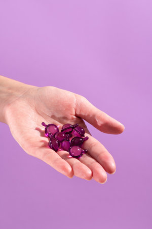 Woman hand holding vitamin capsules in pink, purple colorの写真素材