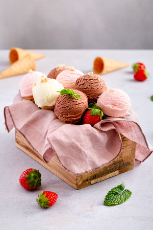 Cones with chocolate, vanilla and strawberry taste in wooden box on light gray tableの写真素材