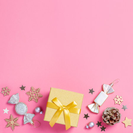 Christmas pink border background with golden gift box with mini Christmas trees and baubles on pastel pink backgroundの写真素材