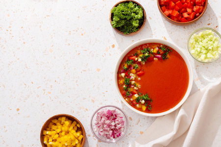 Spanish tomato gazpacho cold soup styled and decorated in white plate with ingredients on white table, top viewの写真素材