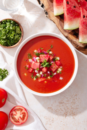 Spanish tomato and watermelon gazpacho cold soup styled and decorated in white plate with ingredients on concrete table in hard light with shadows, top viewの写真素材