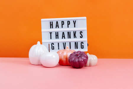 Lightbox with text Happy Thanksgiving with ceramic pumpkins on table, vivid color background.の写真素材