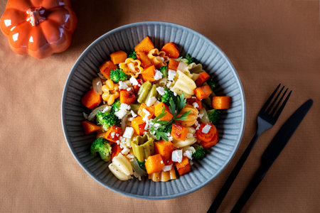 Autumn pasta salad with roasted pumpkin, broccoli, feta cheese on dark wooden background, fall season saladの写真素材