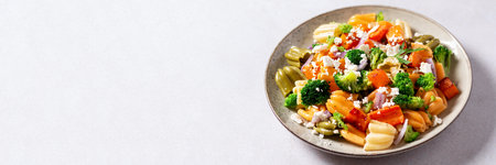 Autumn pasta salad with roasted pumpkin, broccoli, feta cheese on bright light gray background, vivid colors fall season salad, autumn food concept, top view, web banner, copy space.の写真素材