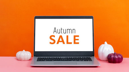 Quote autumn sale on screen laptop on table with minimal autumn or fall season decor, orange colors, seasonal business concept. Decorative ceramic pumpkins and open laptop still lifeの写真素材
