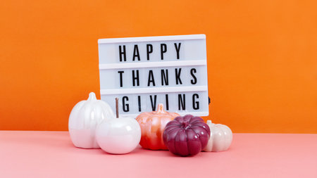 Lightbox with text Happy Thanksgiving with ceramic pumpkins on table, vivid color background. Autumn or fall mock up with seasonal decor still life.の写真素材