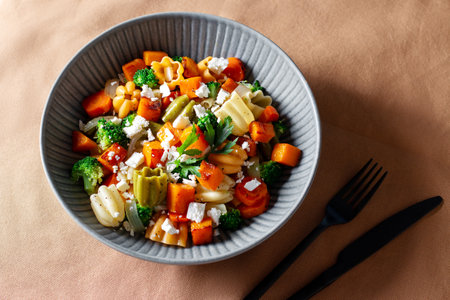 Autumn pasta salad with roasted pumpkin, broccoli, feta cheese on dark wooden background, vivid colors fall season salad, autumn food concept, top viewの写真素材