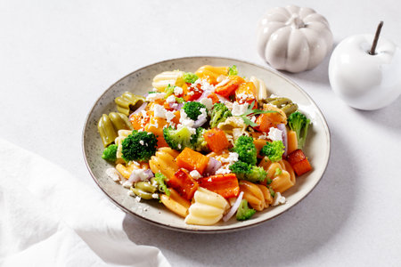 Autumn pasta salad with roasted pumpkin, broccoli, feta cheese on bright light background, fall season saladの写真素材