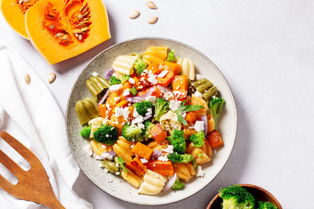 Autumn pasta salad with roasted pumpkin, broccoli, feta cheese on bright light background, fall season saladの写真素材