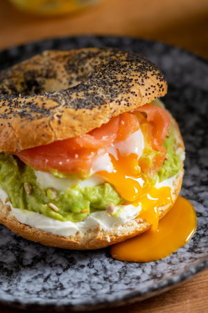 Bagel with poached eggs, cream cheese, avocado, and fish. A cozy and nutritious breakfast or brunch on a wooden tableの写真素材