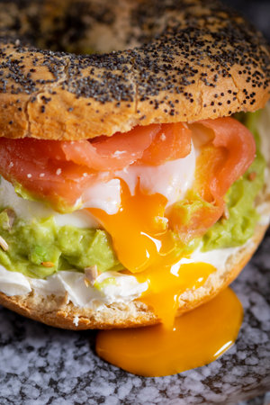 Bagel with poached eggs, cream cheese, avocado, and fish. A cozy and nutritious breakfast or brunch on a wooden tableの写真素材