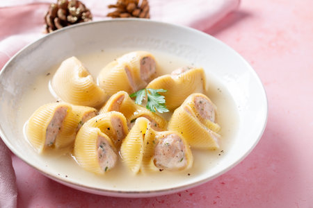 Traditional Catalan Christmas dish Escudella in white plate on pink table, stuffed pasta in meat broth, top viewの写真素材