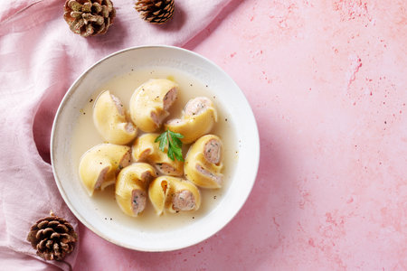 Traditional Catalan Christmas dish Escudella in white plate on pink table, stuffed pasta in meat broth, top view, copy spaceの写真素材