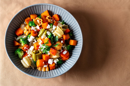 Autumn pasta salad with roasted pumpkin, broccoli, feta cheese on dark wooden background, vivid colors fall season salad, autumn food concept, top viewの写真素材